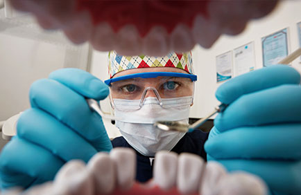 Dra. Débora Reis – Prótese Dentária Dentista examinando prótese dentária do ponto de vista do paciente, com instrumentos em mãos