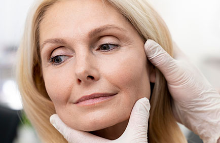 dra-debora-reis-procedimentos-bichectomia-2 Profissional examinando o contorno facial de paciente madura durante consulta para bichectomia