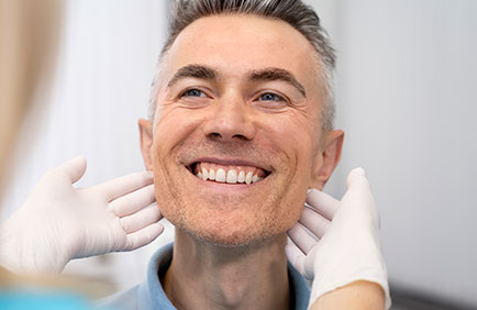 Dra Debora Reis – Gengivoplastia Homem sorridente sendo avaliado por dentista após procedimento de gengivoplastia
