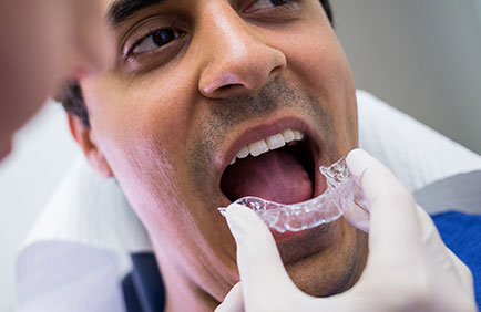 Dra Debora Reis – Ortodontia com Invisalign Dentista auxiliando paciente homem a colocar alinhador Invisalign durante consulta.