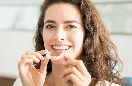 Dra Debora Reis – Ortodontia com Invisalign Mulher sorridente segurando alinhador Invisalign em consultório odontológico.