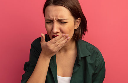 Dra Debora Reis – Periodontia Mulher cobrindo a boca por desconforto causado por mau hálito ou inflamação gengival