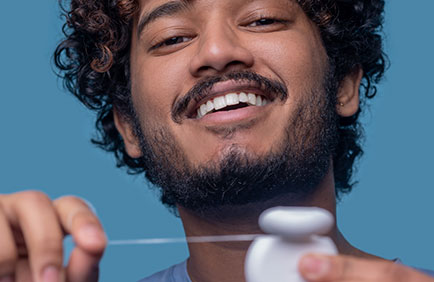 Dra Debora Reis – Periodontia Homem sorrindo com fio dental nas mãos, reforçando a importância da higiene bucal preventiva